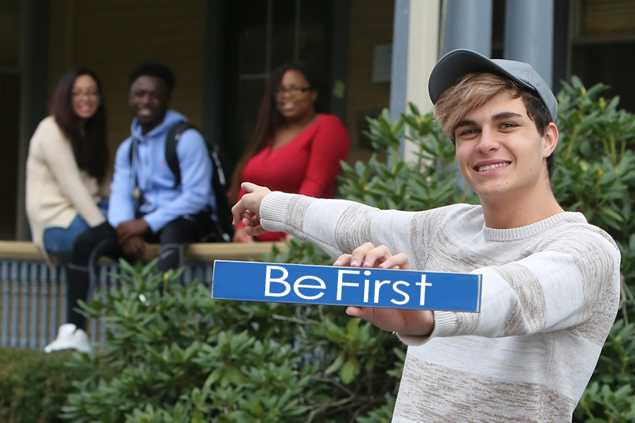 first-generation student smiles and holds a sign that reads Be First.