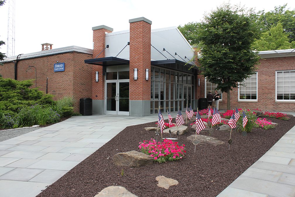 Front entrance of Hibbard Center decorated with American flags and red and pink flowers,